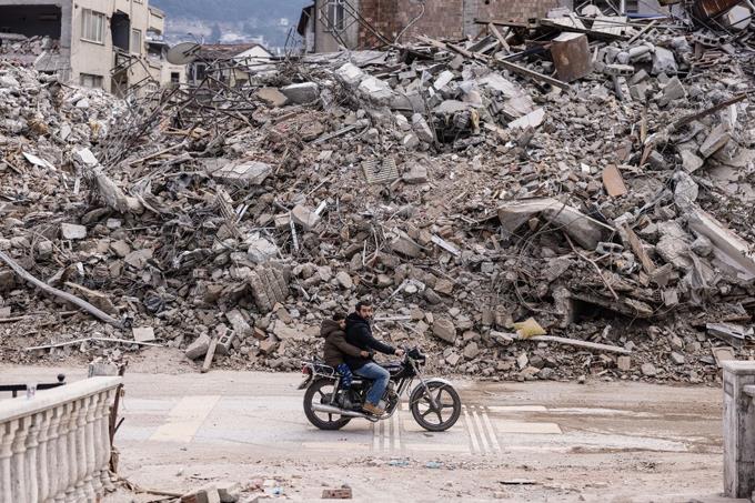 Un hombre conduce su motocicleta frente a edificios derrumbados en la ciudad de Antakya el 19 de febrero de 2023.